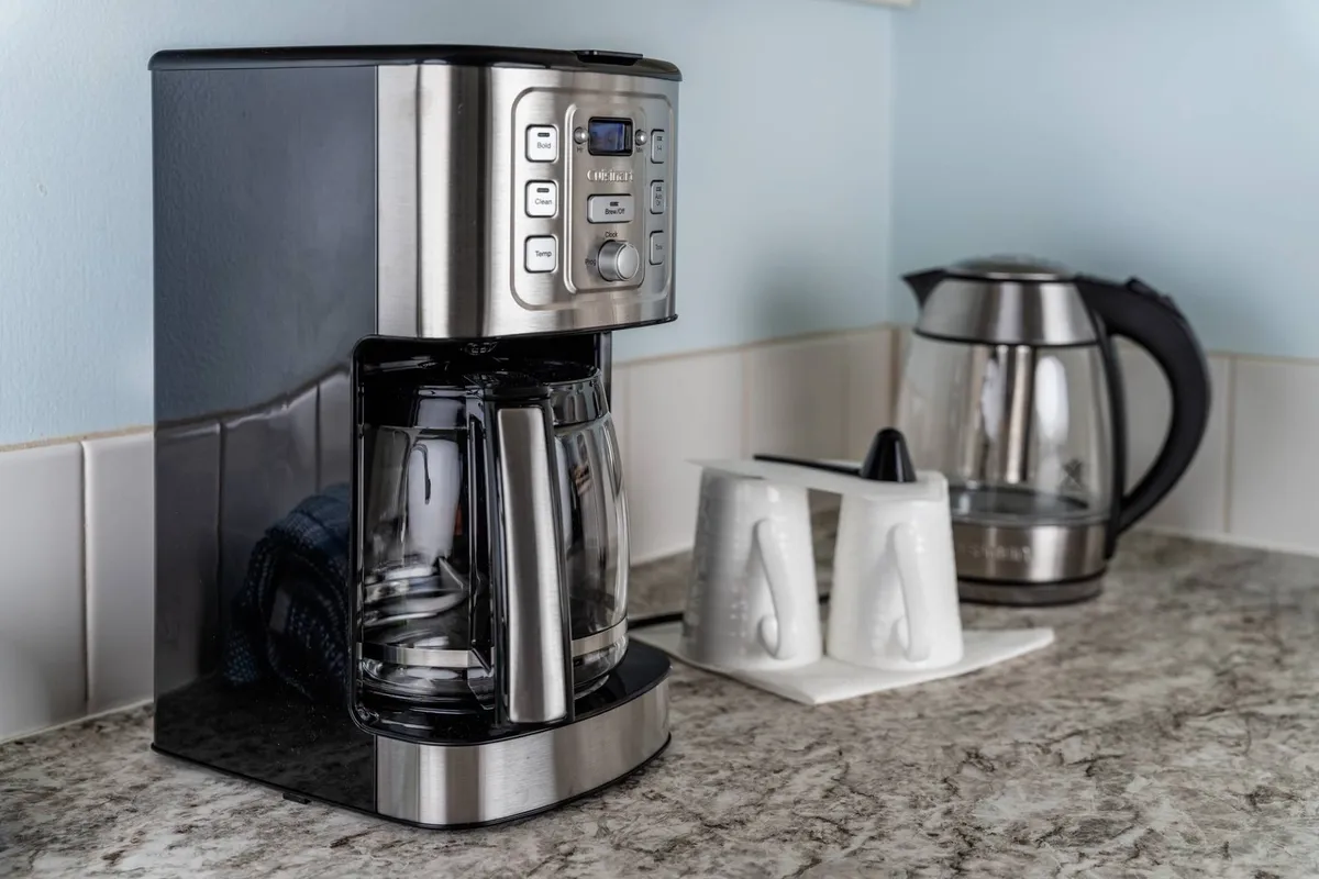 A cozy coffee nook featuring a coffee maker, electric kettle, and ceramic cups, set on a kitchen counter. The scene invites morning rituals and casual conversations, highlighting both functionality and comfort.