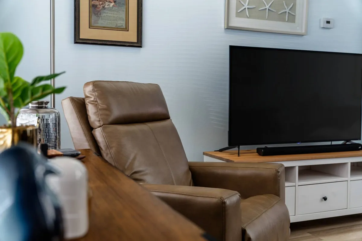 A cozy corner featuring a modern leather armchair, a large television mounted at eye level, tasteful wall art, and a healthy indoor plant. The space feels both polished and homey, with thoughtful decorative elements that add to the sense of comfort.