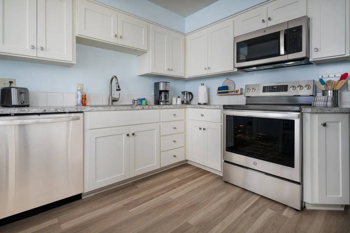 This interior image features a welcoming kitchen with stainless steel appliances, granite countertops, and white cabinetry. The scene conveys a sense of warmth and togetherness, evoking moments of cooking and gathering with family or friends. The modern appliances are clearly visible, and the open kitchen space encourages connection and activity.