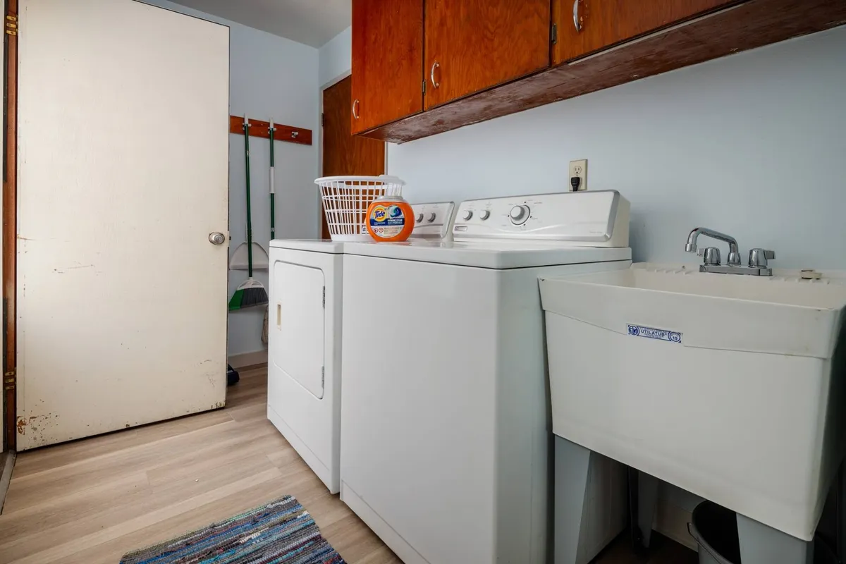 A neatly organized laundry area featuring a modern washing machine and drying machine, a utility sink, and a laundry basket. The space is bright, clean, and conveys a sense of convenience and home functionality.