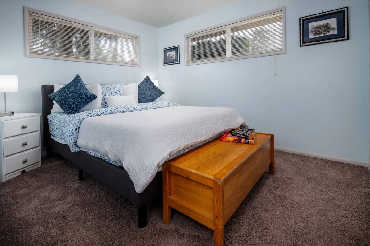 This interior photo showcases a tranquil bedroom featuring a neatly made bed topped with decorative pillows, a wooden bench at the foot, and a softly glowing nightstand lamp. The inviting color palette and thoughtfully placed lighting evoke a calm, restful ambiance.