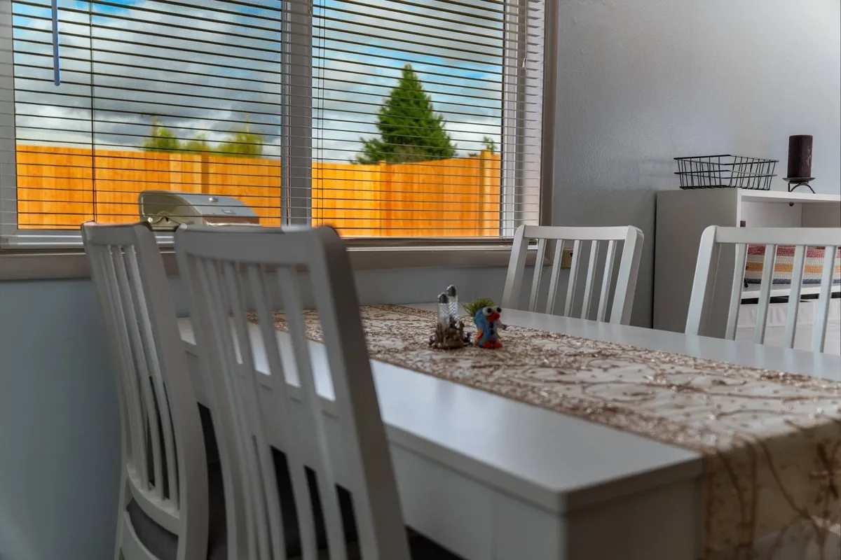 A dining area with a prominent table set near a window, adorned with decorative items. The warm, welcoming mood is enhanced by natural light, making it an ideal setting for shared meals, laughter, or late-night games. The open space suggests easy movement between kitchen and dining zones.