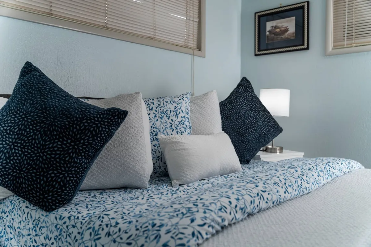 A serene bedroom setting with neatly arranged decorative pillows, a plush bedspread, and a softly glowing nightstand lamp. The atmosphere is tranquil and welcoming, ideal for relaxation after a busy workday.